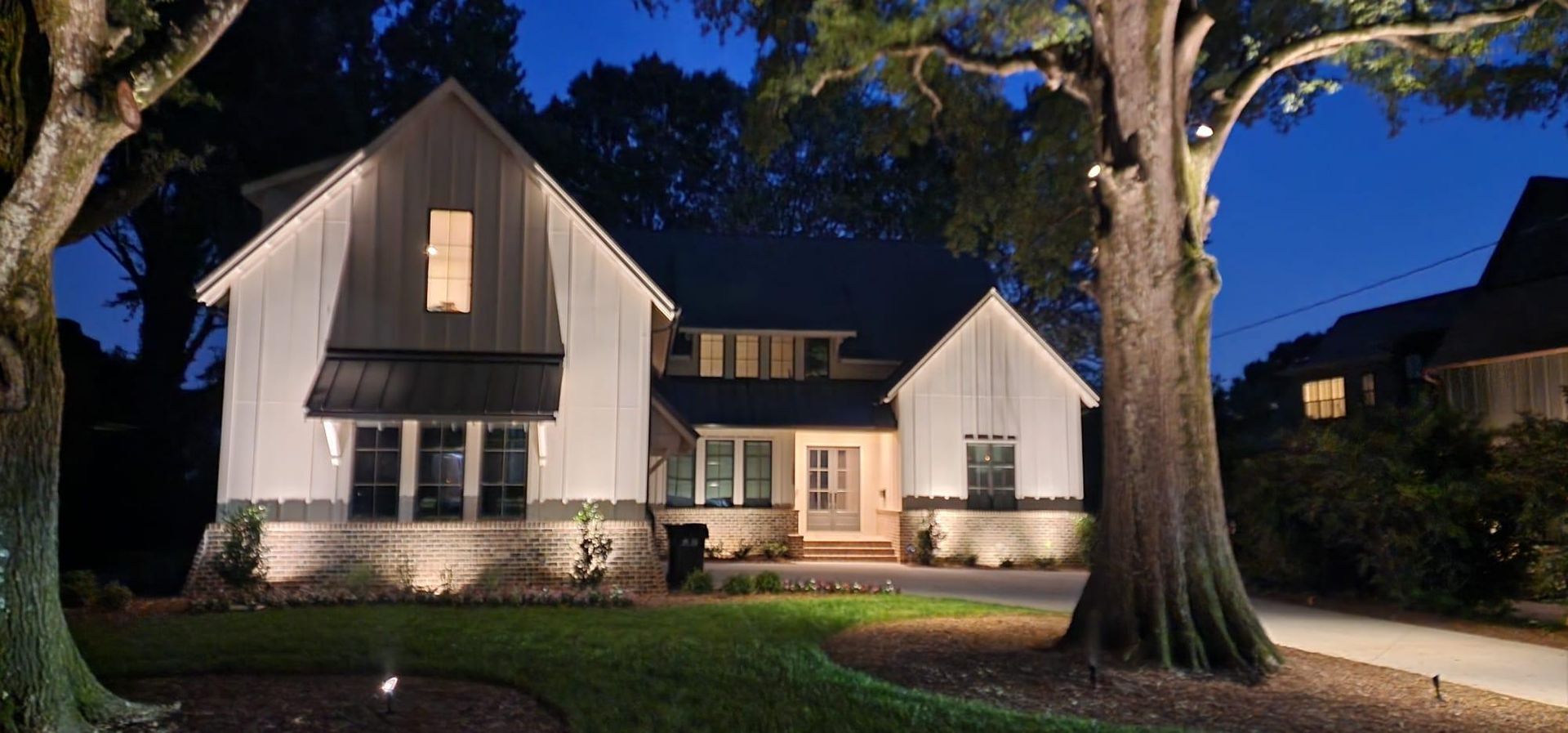 A well-lit house at night with a yard and trees.