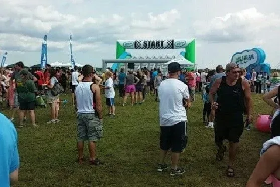 Crowd at a race, people gathered in front of an inflatable finish line arch on a grassy field under a cloudy sky.