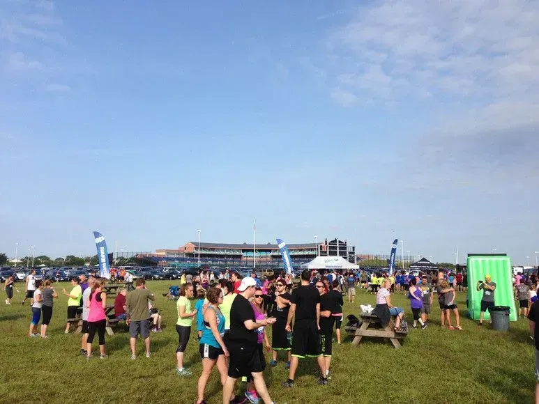 Large crowd of people gathered outdoors on a grassy field, likely before a race or event.