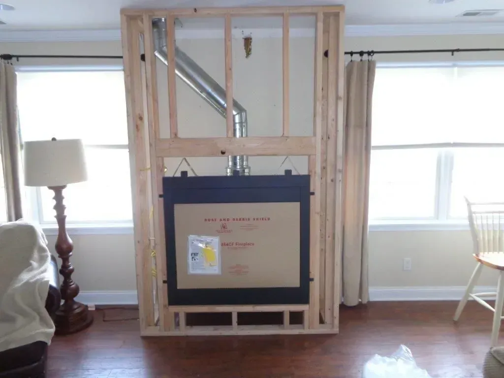 Wooden frame built around a fireplace, between two windows. The fireplace is not finished.