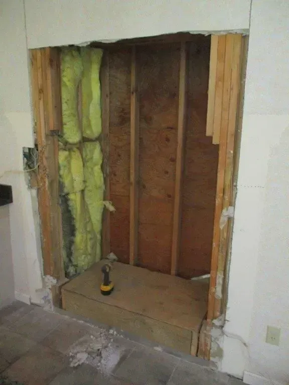 A partially demolished wall reveals studs, insulation, and a plywood base, likely for a fireplace or cabinet.