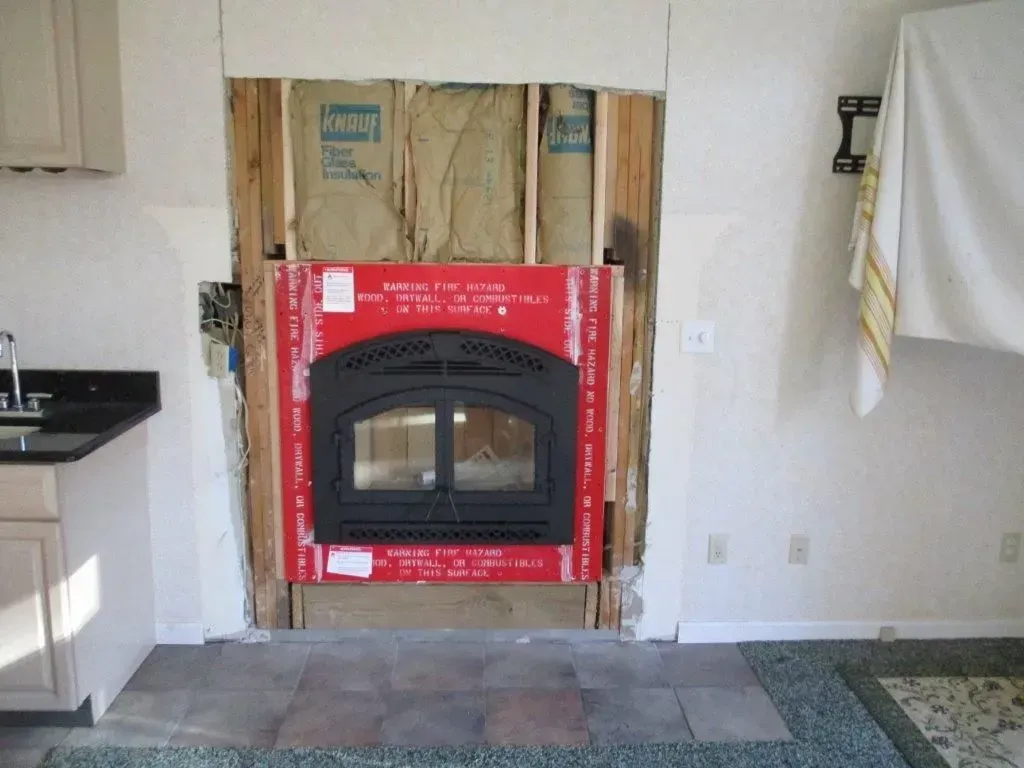 Fireplace installation: wood frame, insulation, and black fireplace insert in a wall.