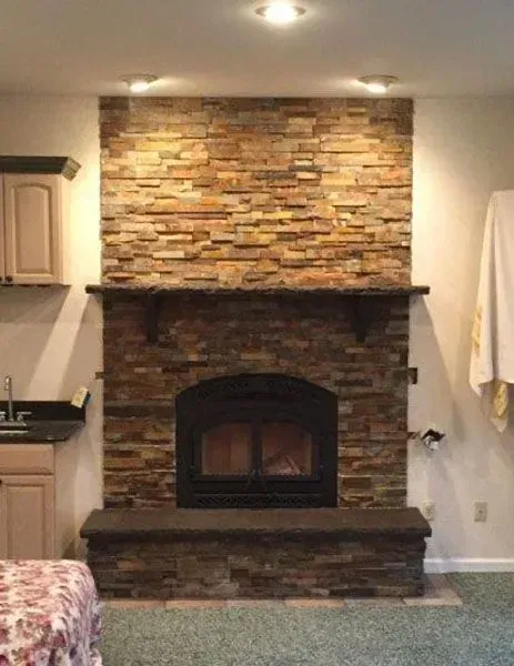Fireplace with stone surround, dark hearth and mantel, built-in in a room with light walls, cabinets, and green carpet.