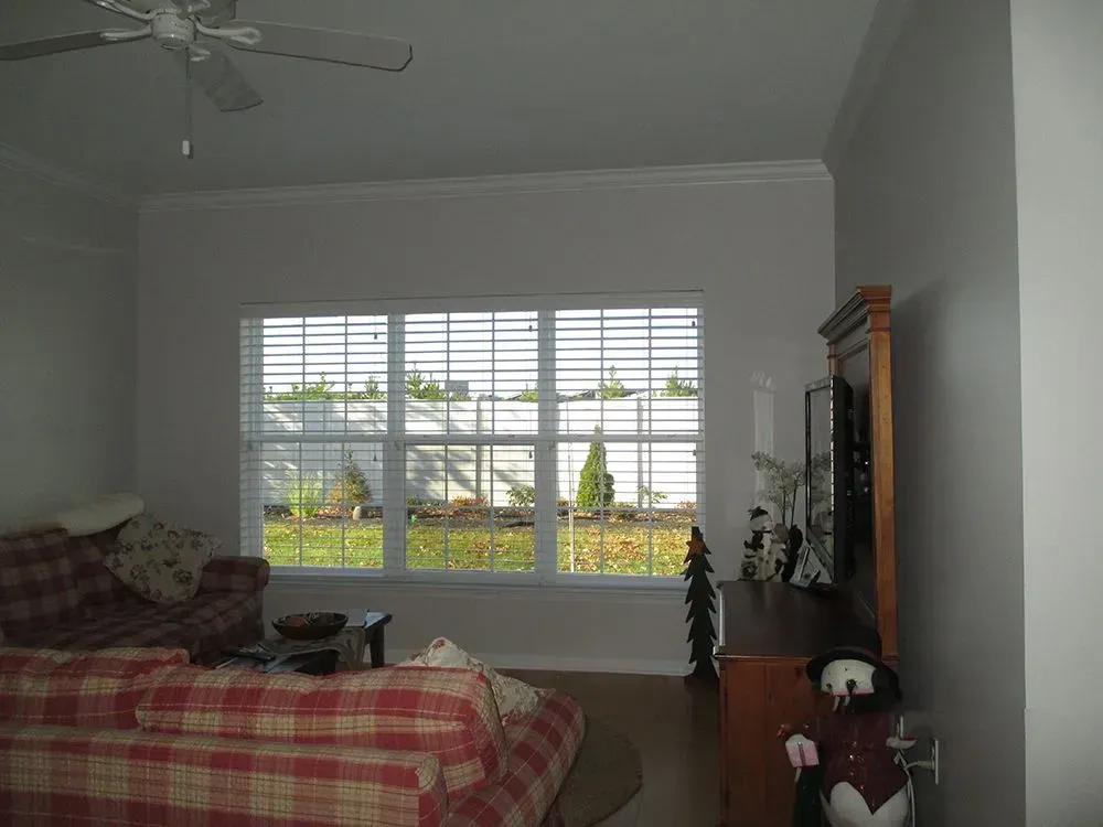 Living room with a plaid sofa, window with blinds, and a cabinet with decorations.