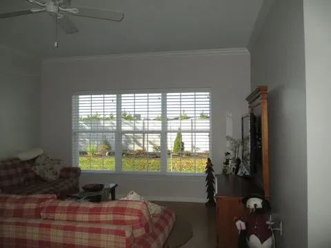 Living room with a plaid sofa, window with blinds, and a cabinet with decorations.
