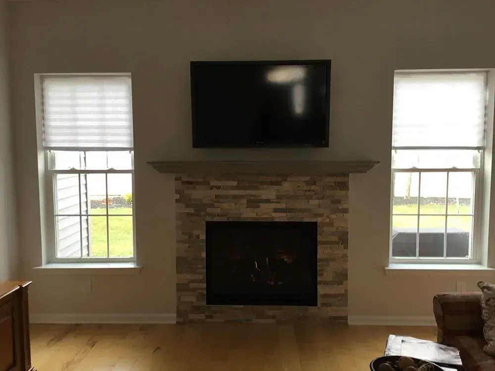Fireplace with a mounted TV, flanked by two windows with shades. The setting is a living room.
