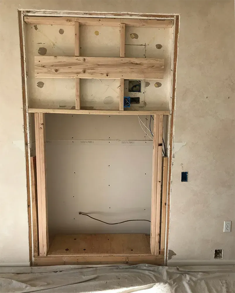 Wooden frame in a wall, likely for a fireplace or media center, under construction.