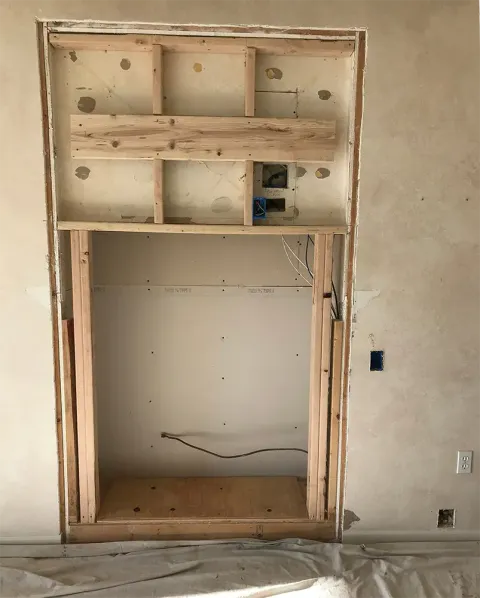 Wooden frame in a wall, likely for a fireplace or media center, under construction.