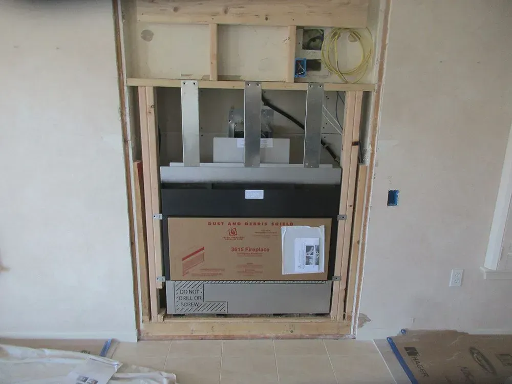 Fireplace unit installed in a framed wall opening, with visible cardboard packaging and electrical components.