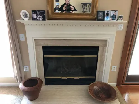 Fireplace with decorative items on the mantel and floor, person reflected in the mirror above.
