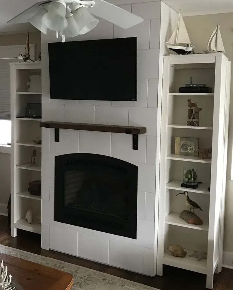 White fireplace with a TV above, flanked by white bookshelves; nautical decor on shelves.