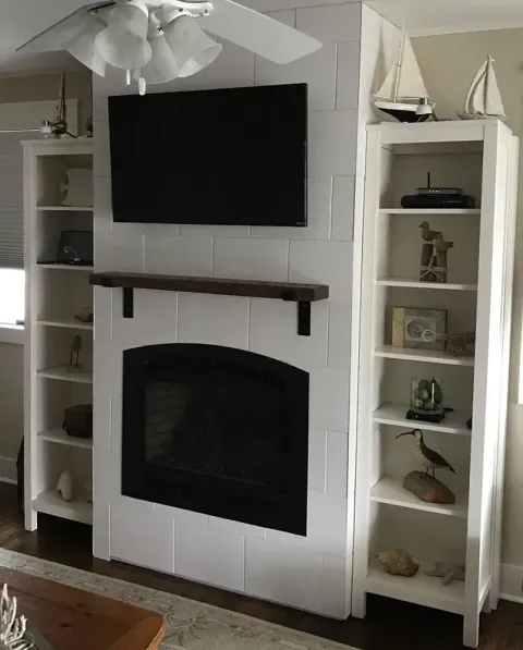 White fireplace with a TV above, flanked by white bookshelves; nautical decor on shelves.