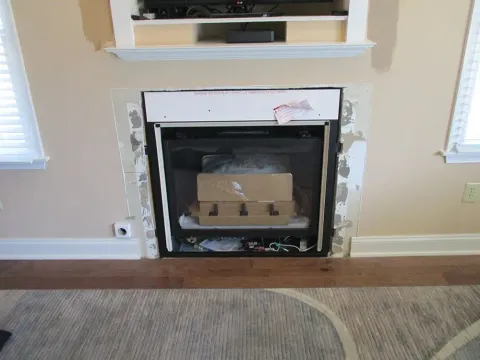 Fireplace with removed surround and objects inside the firebox, set in a light-colored room.