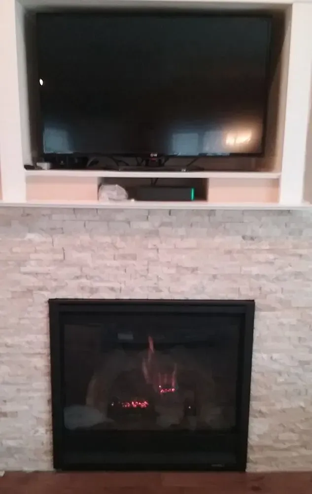 Fireplace with lit flames below a large TV mounted in a white-walled alcove.