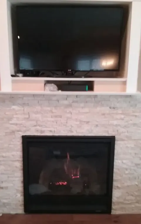 Fireplace with lit flames below a large TV mounted in a white-walled alcove.
