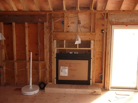 Interior framing with fireplace insert; wires exposed, unfinished construction.