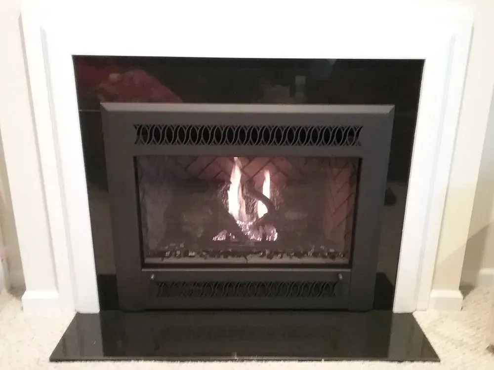 Gas fireplace with black surround, white frame, and flames.