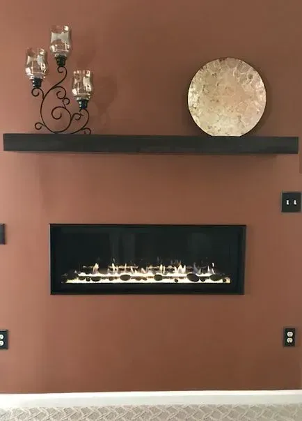 Fireplace on brown wall with dark shelf holding candle holder and decorative plate.