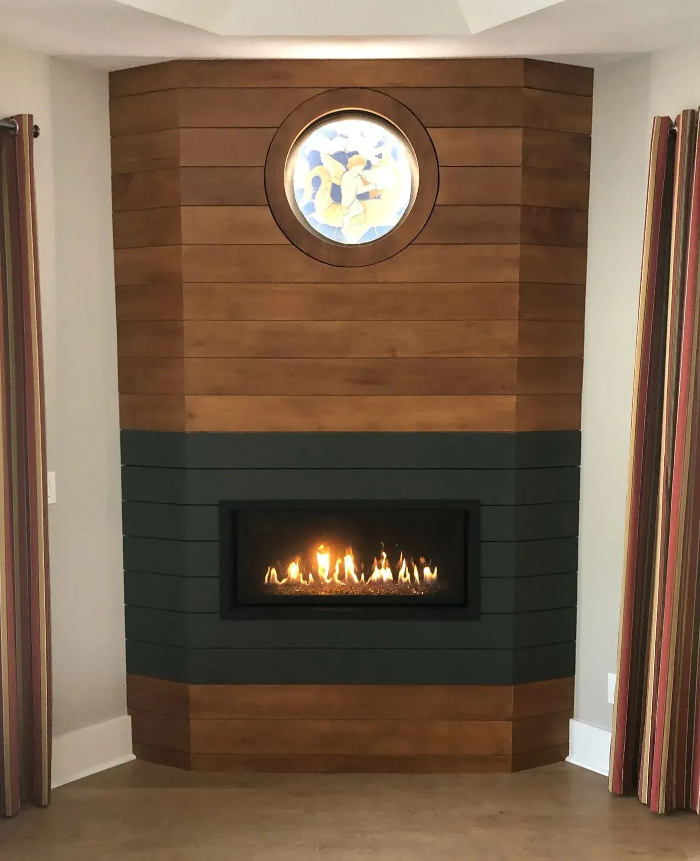 Fireplace with wood paneling, a stained glass window, and a burning flame.