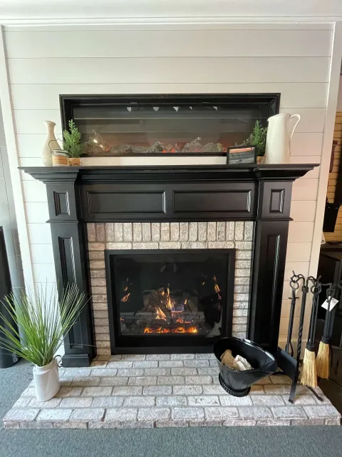Black fireplace mantel with brick surround and decorative items.