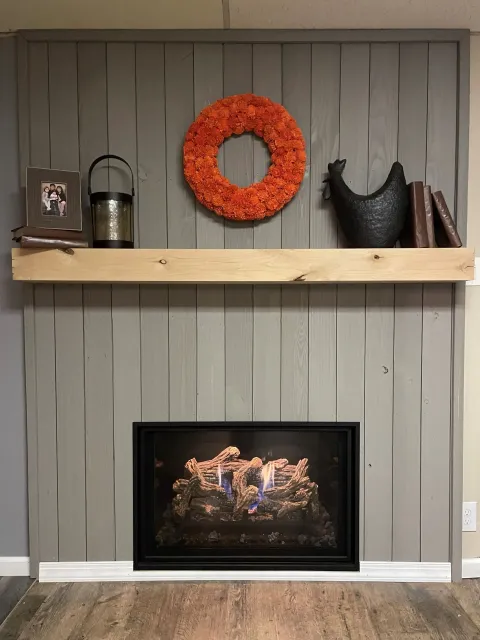 Gray painted fireplace with a wooden shelf holding decor, including an orange wreath.