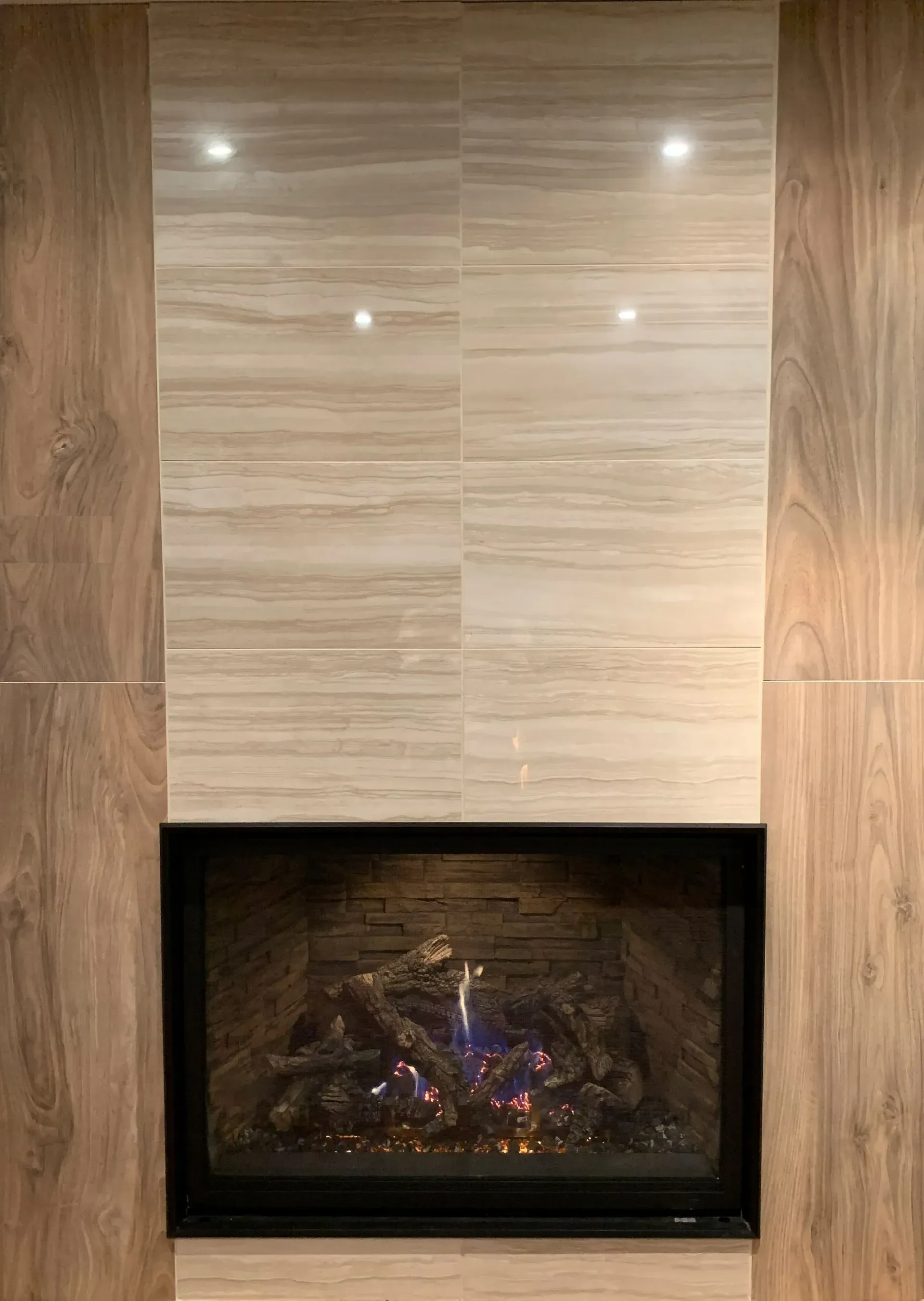 Fireplace with a beige and brown tiled surround. The fireplace is dark, with glowing faux logs.