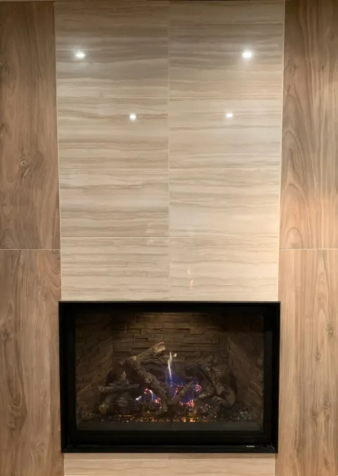 Fireplace with beige marble tile surround flanked by wood-look panels, modern design.