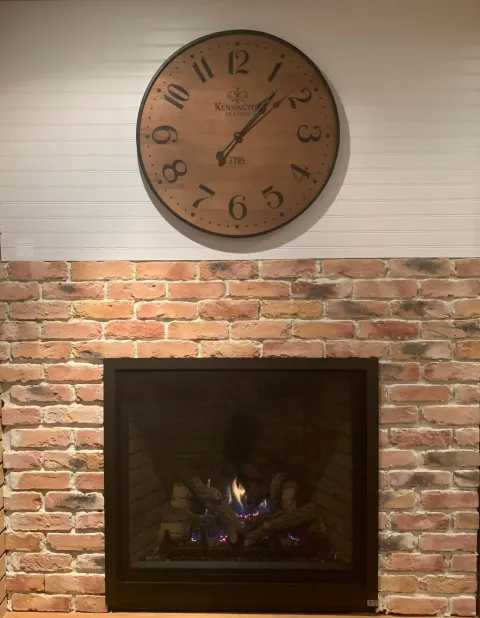 Clock above a brick fireplace with a fire burning.