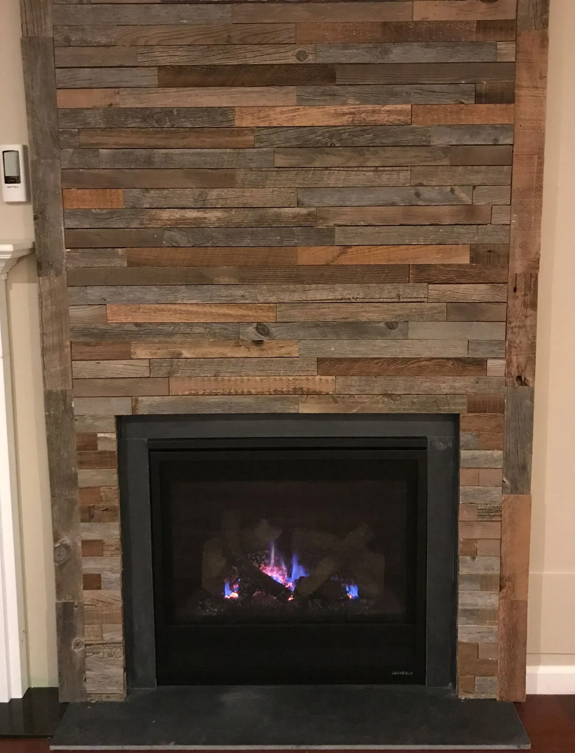 Fireplace with rustic wood panel surround, black firebox, and glowing blue flames.