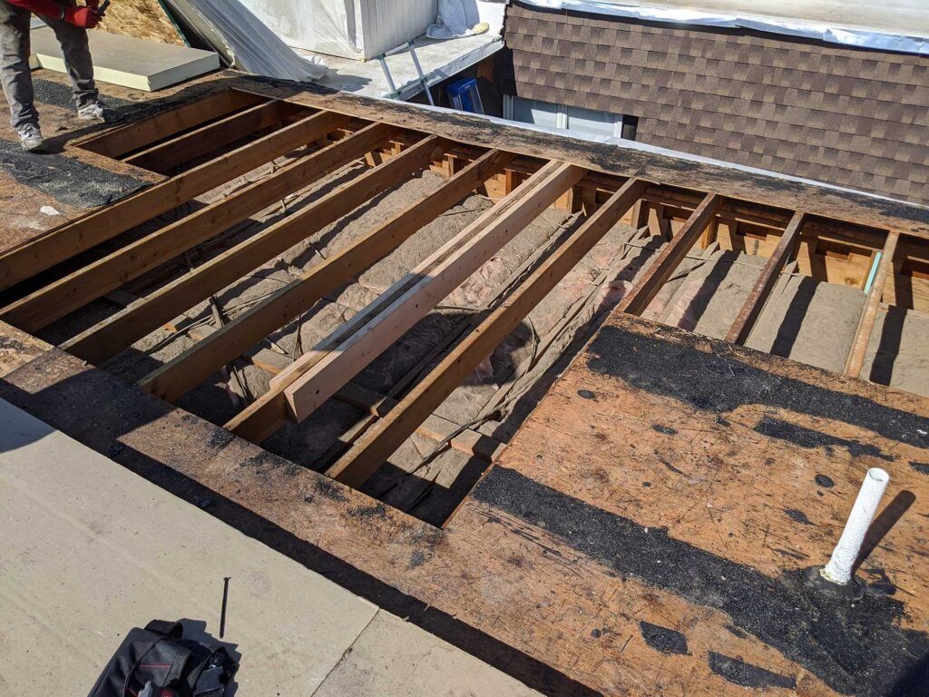 Roof under construction, showing exposed beams and a partially removed surface. Person standing nearby.