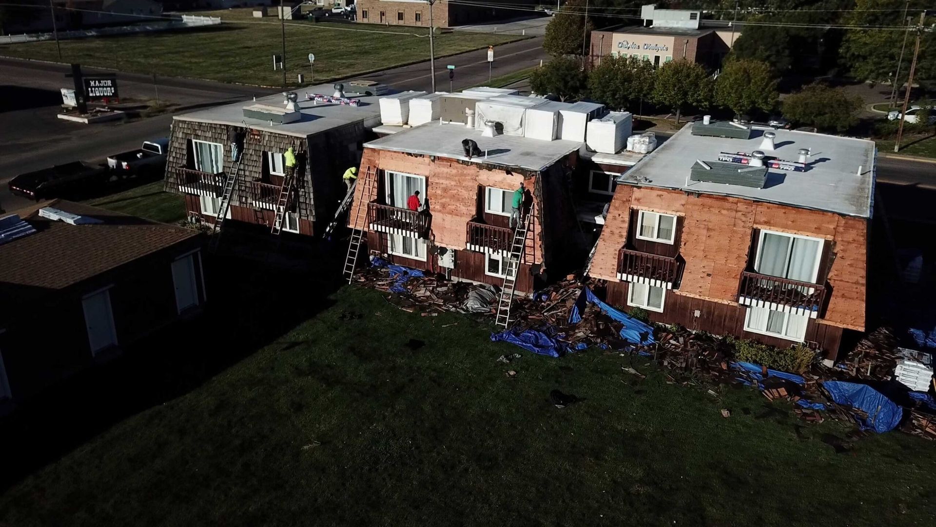 Three damaged brick apartment buildings on a grassy hill, debris scattered below.
