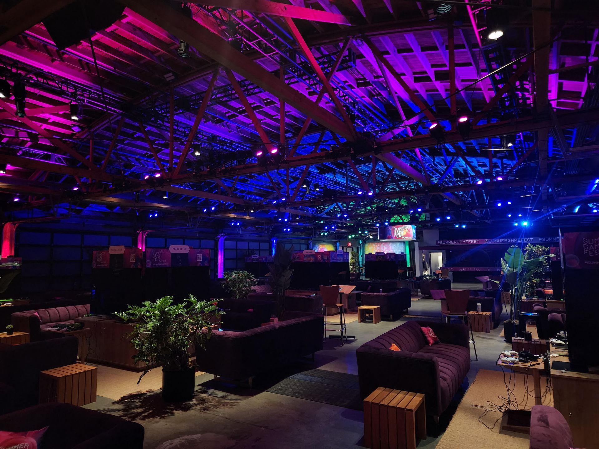 Dim lounge with sofas and plants under vivid purple and blue ceiling lights