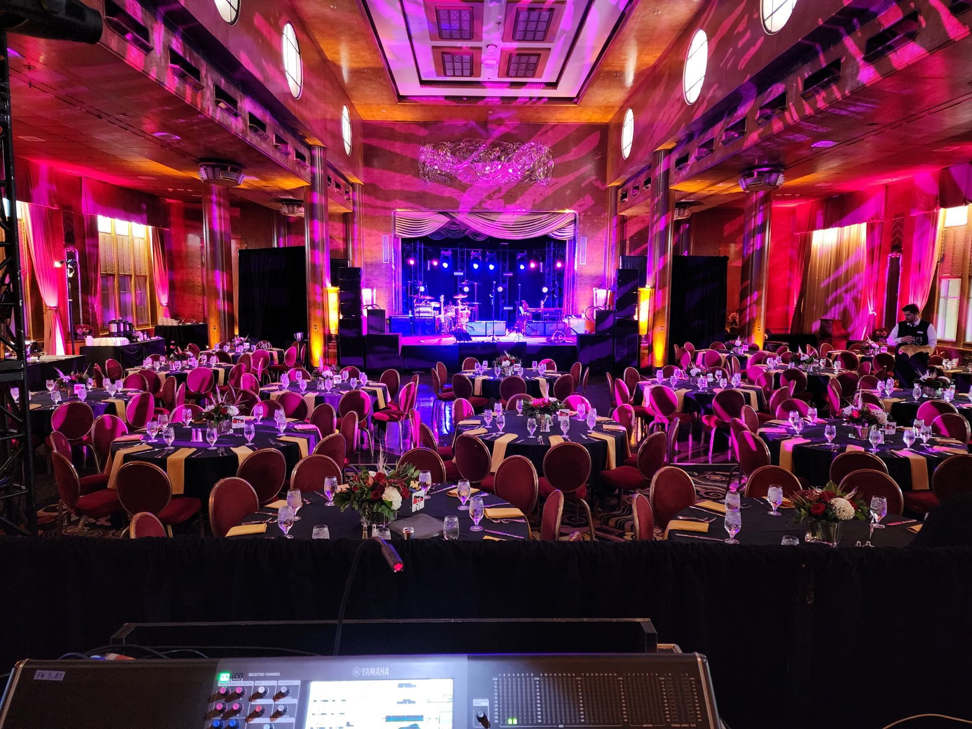Crowded banquet hall with pink and purple lighting facing a lit stage