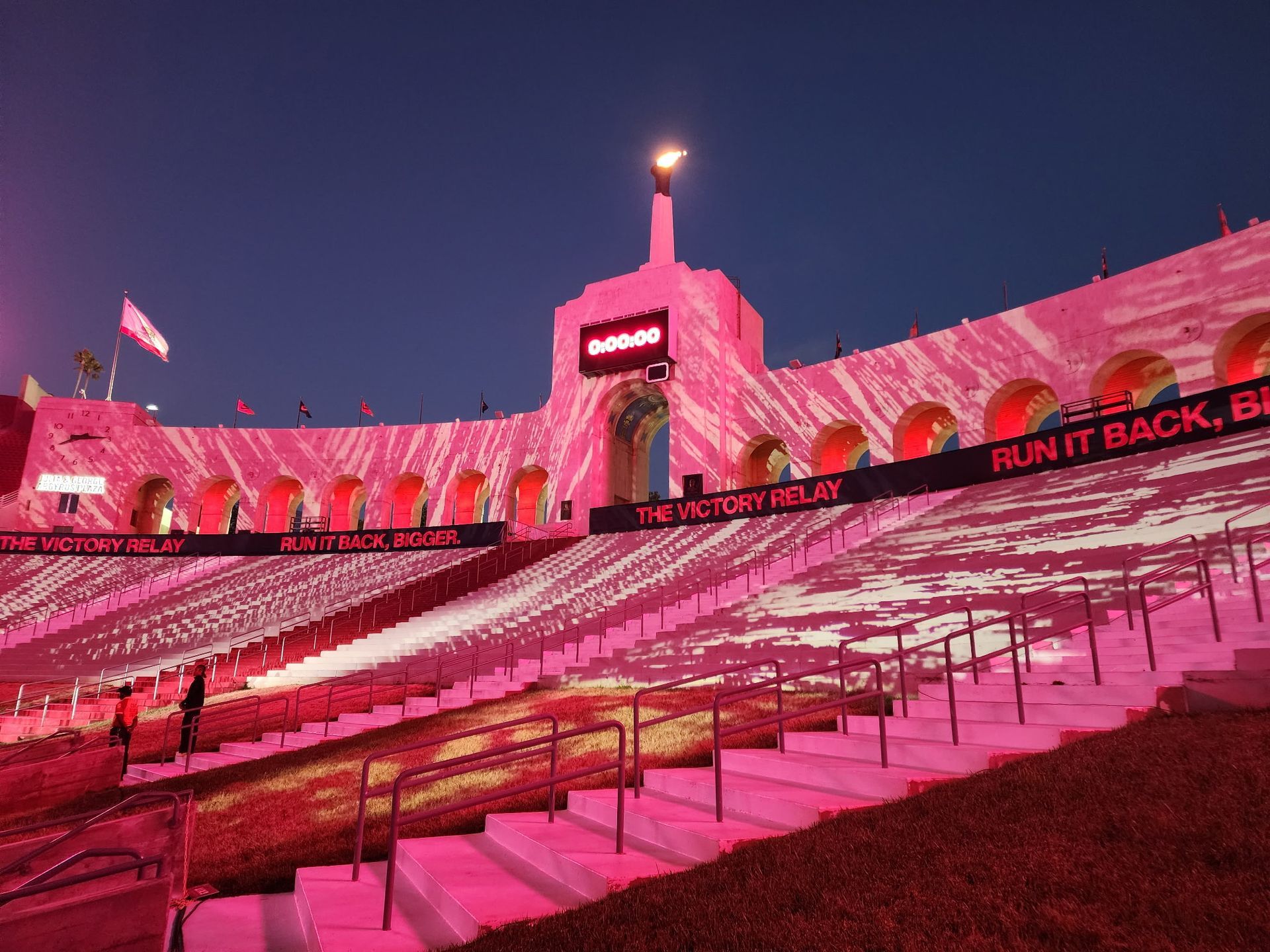 Pink-lit stadium stands at night with a torch glowing atop the center tower.