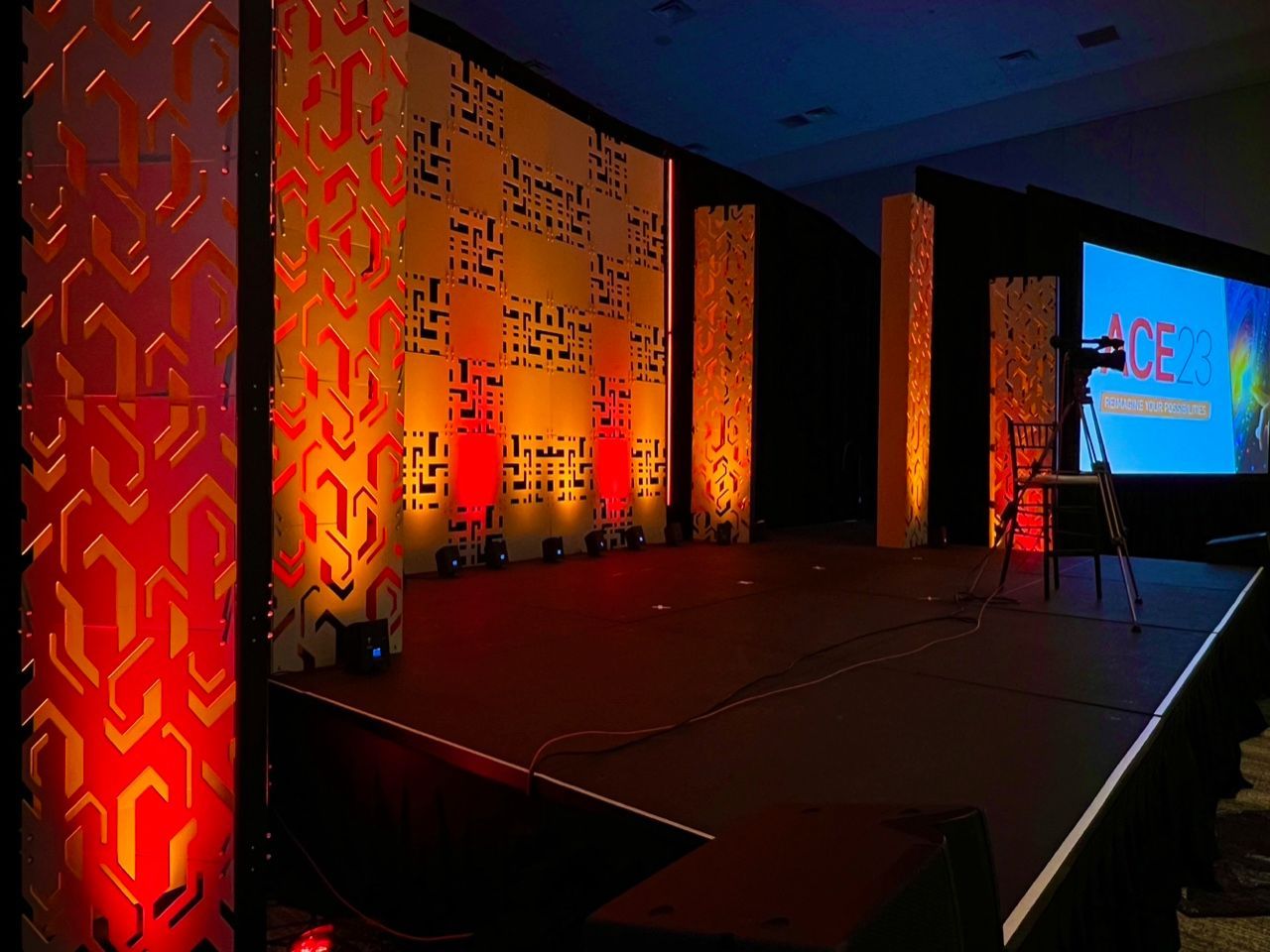 Empty lit stage with patterned orange panels and a blue presentation screen in a dark conference room