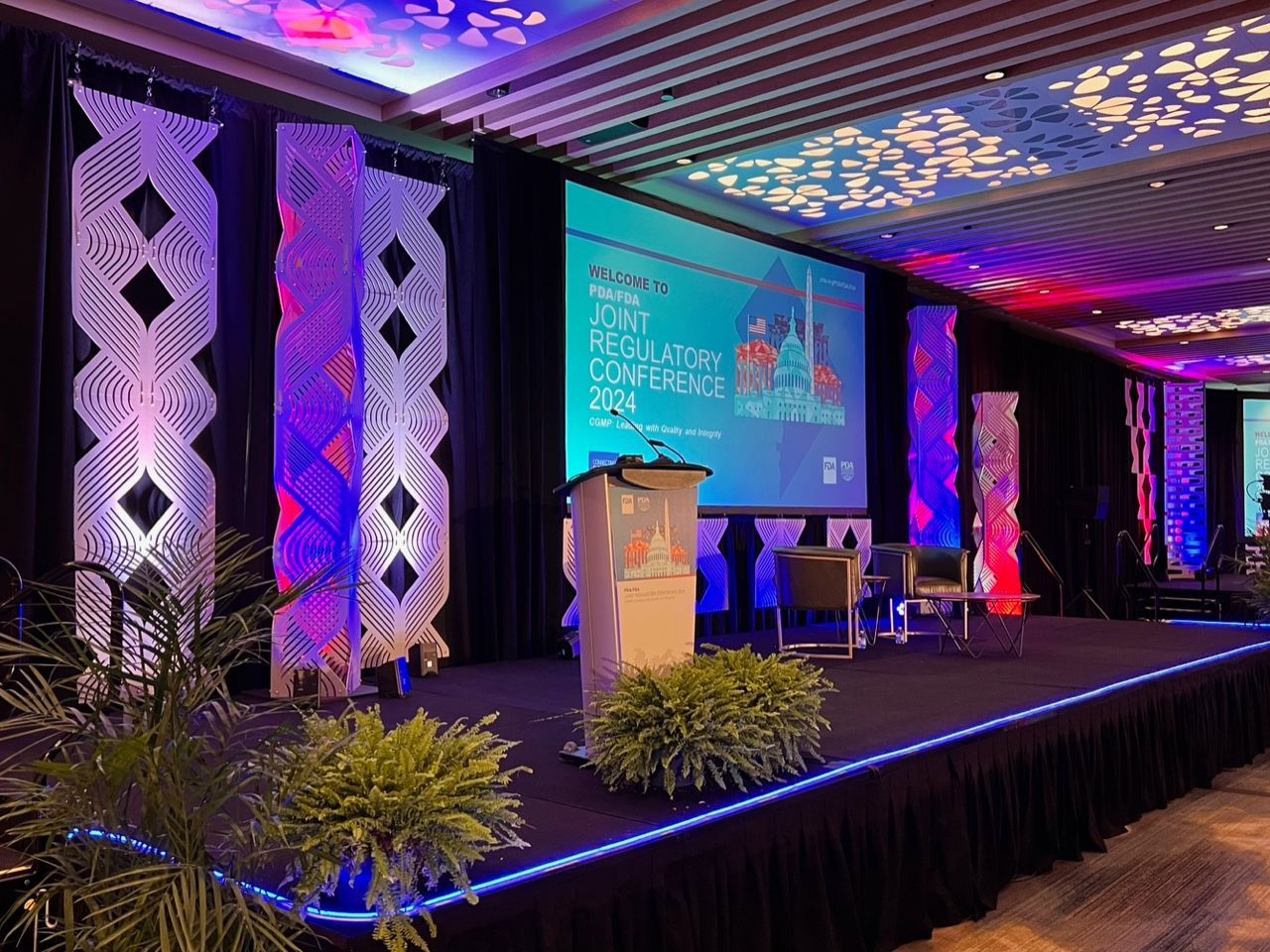 Conference stage with purple lighting, podiums, and a presentation screen in a decorated ballroom