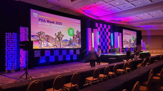 Conference hall with purple lighting, large screens, and rows of chairs facing a stage