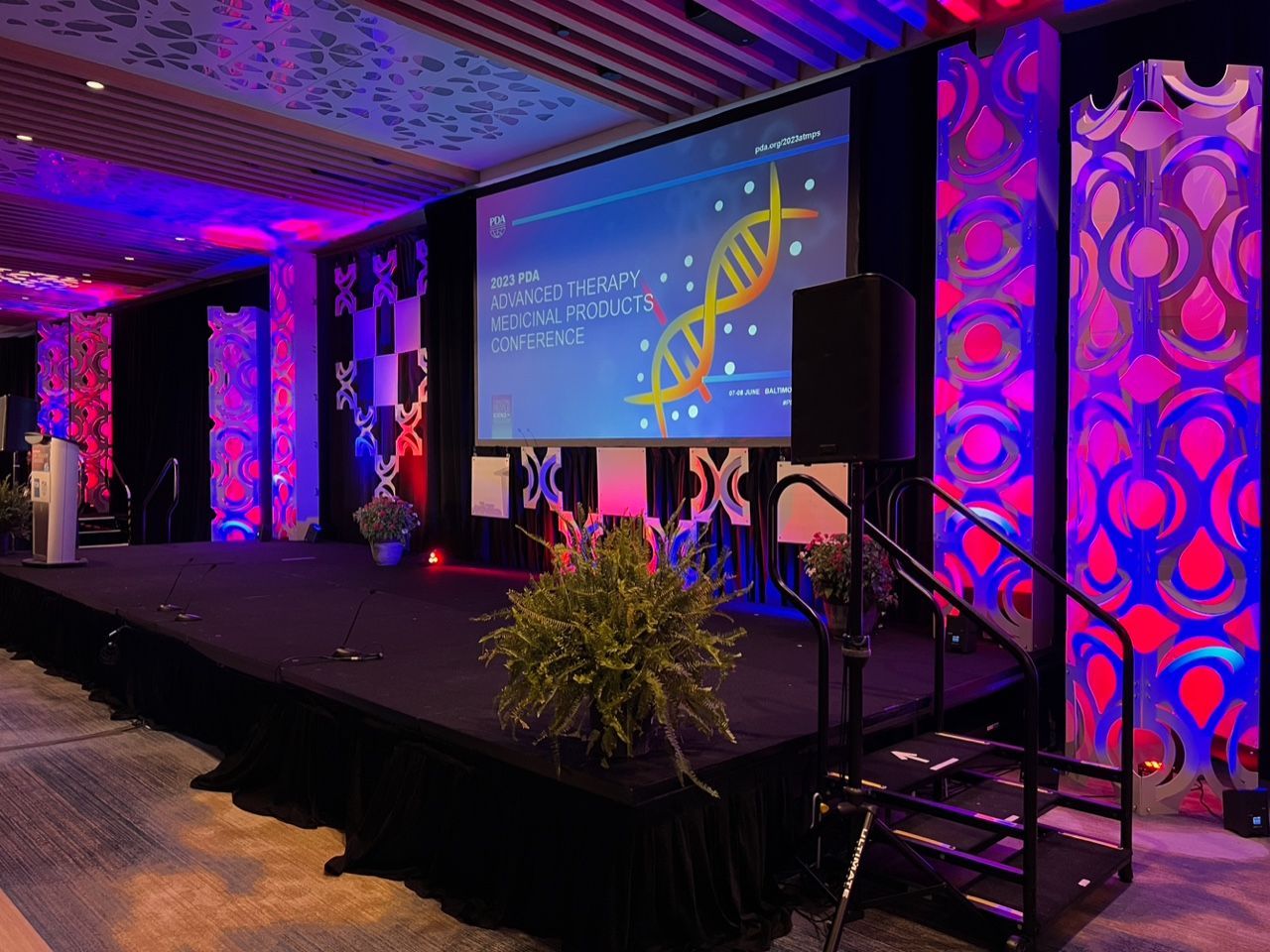 Stage setup with large screen, purple lighting, and patterned columns in a conference hall