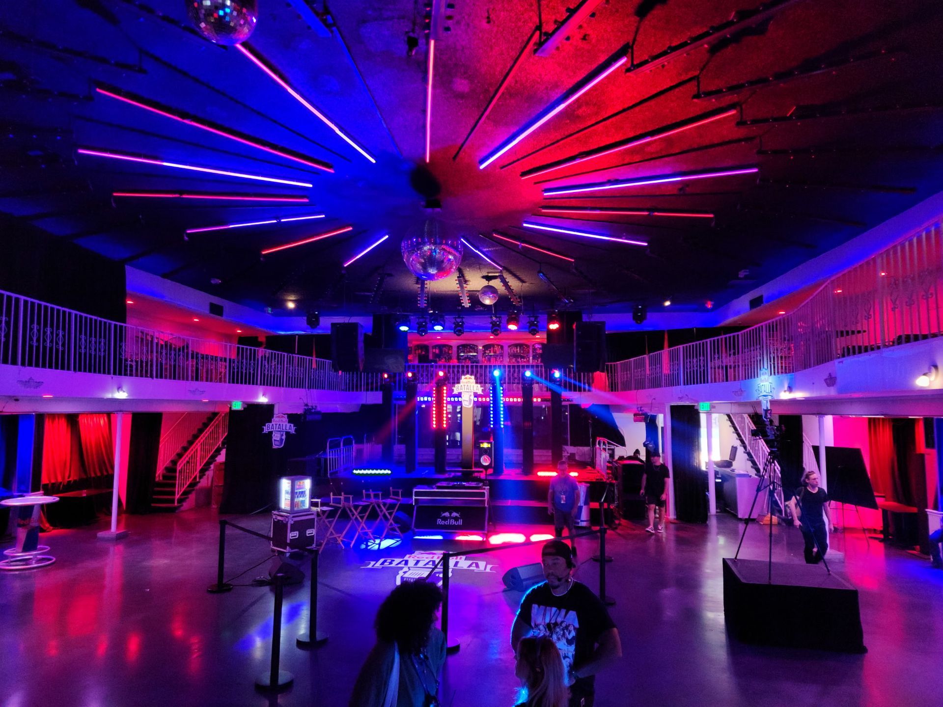 Neon-lit nightclub interior with red and blue lights, central dance floor, and a glowing ceiling installation