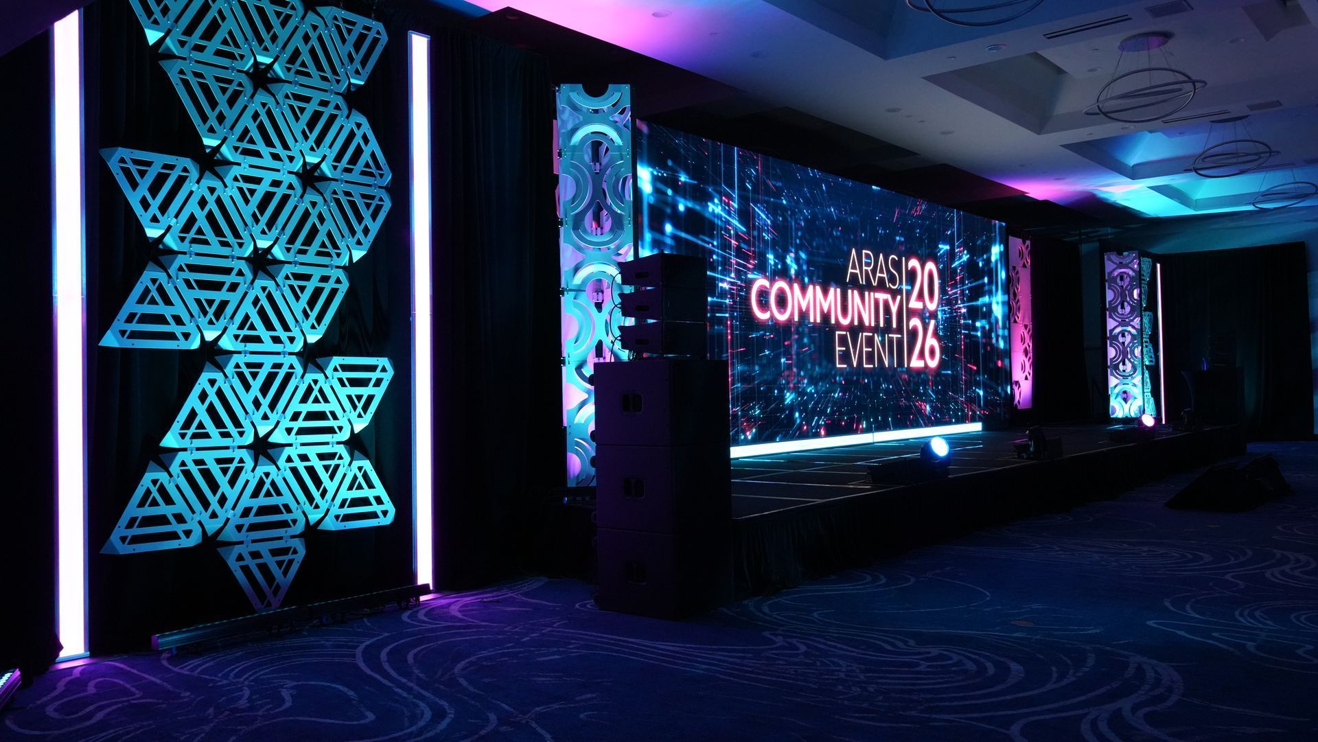 Neon-lit conference stage with glowing geometric wall art and a large screen reading “COMMUNITY.”