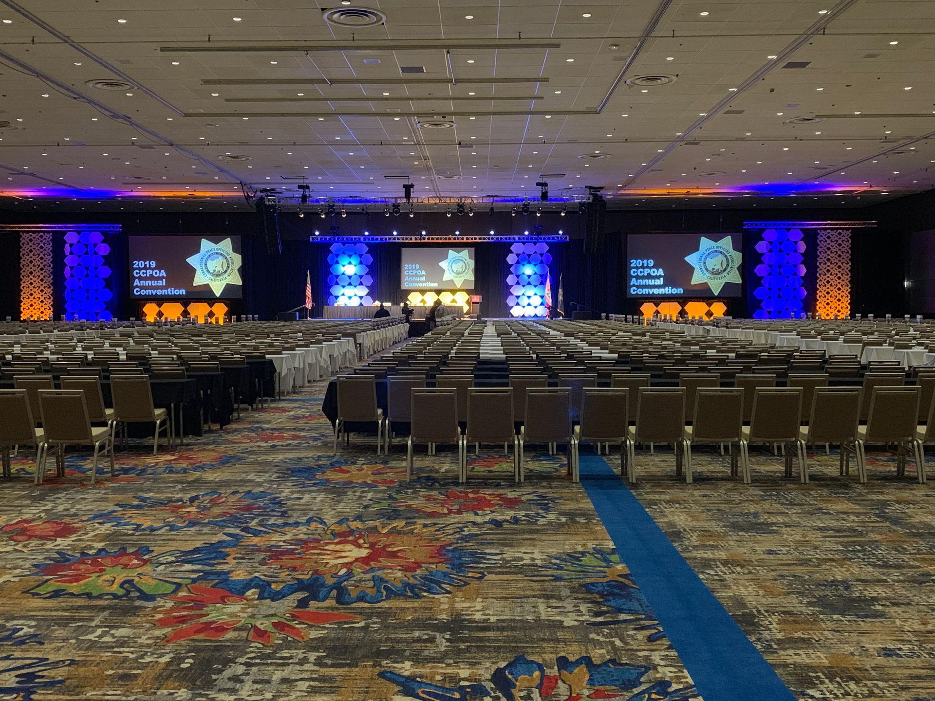 Conference hall with stage, multiple large screens, rows of chairs, and colorful patterned carpet