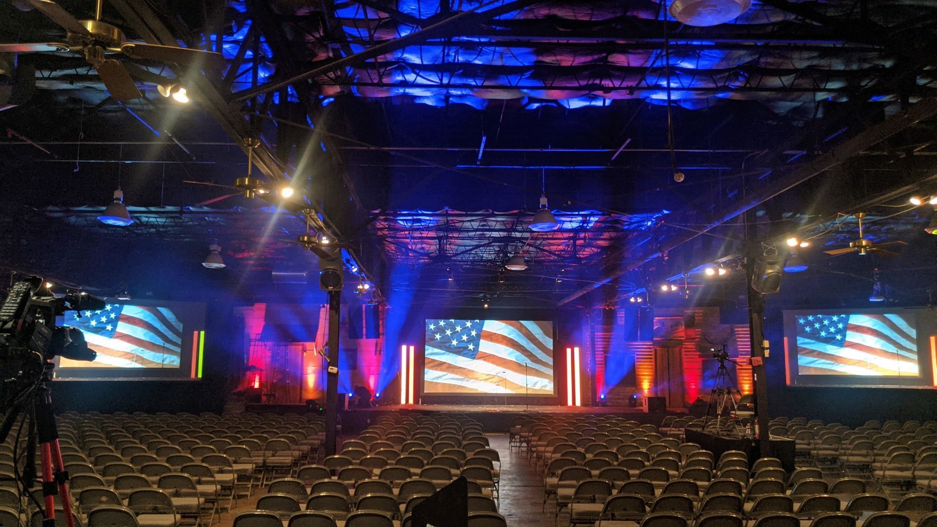 Empty auditorium with rows of chairs facing a lit stage with blue, red, and orange screens and uplighting