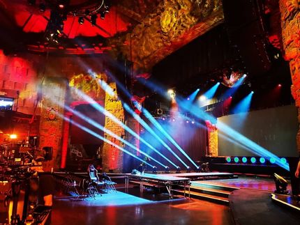 A brightly lit stage with red textured walls, illuminated by rows of sharp blue spotlights angled toward the floor.