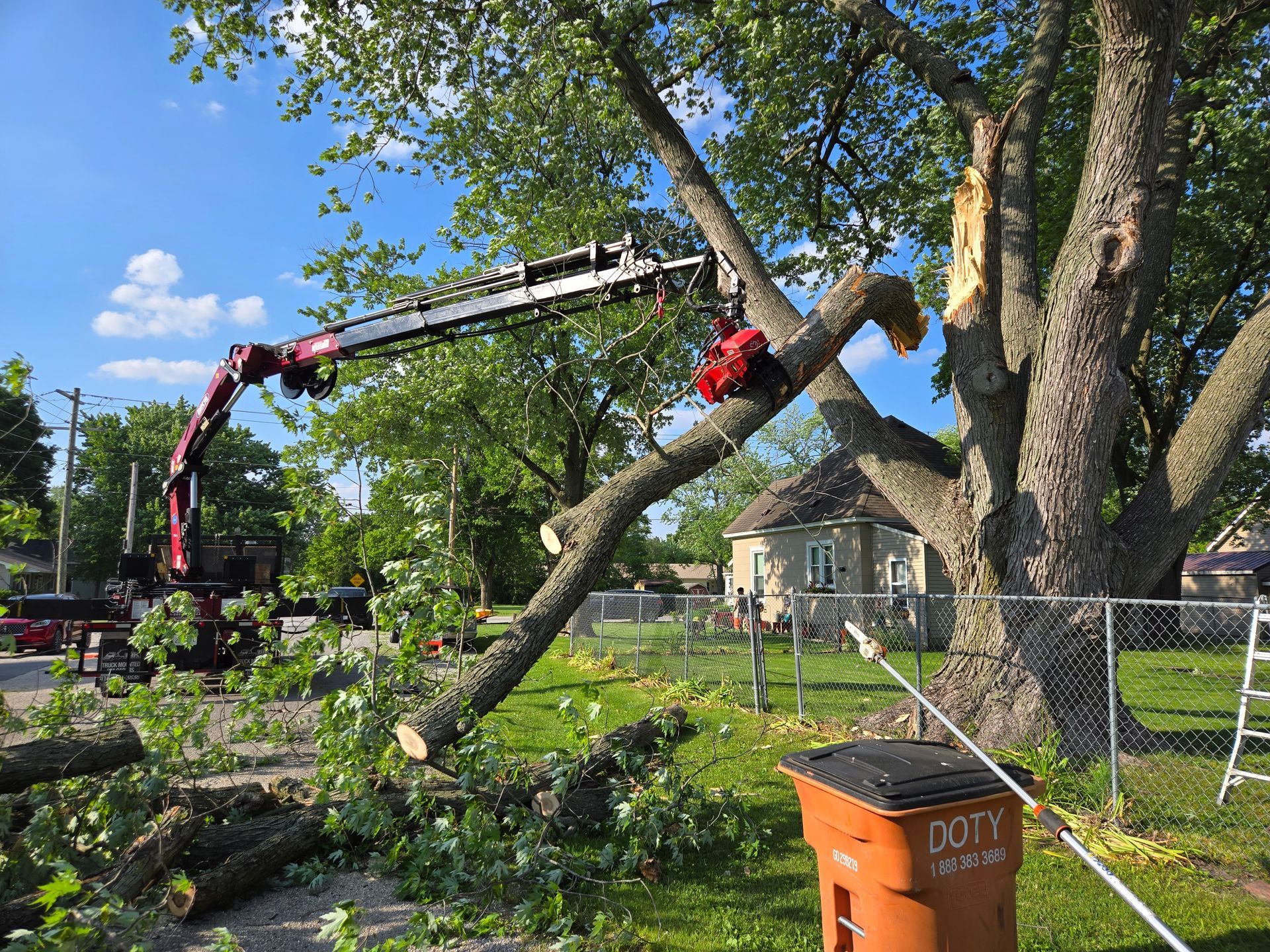 A crane is cutting down a tree in a yard.
