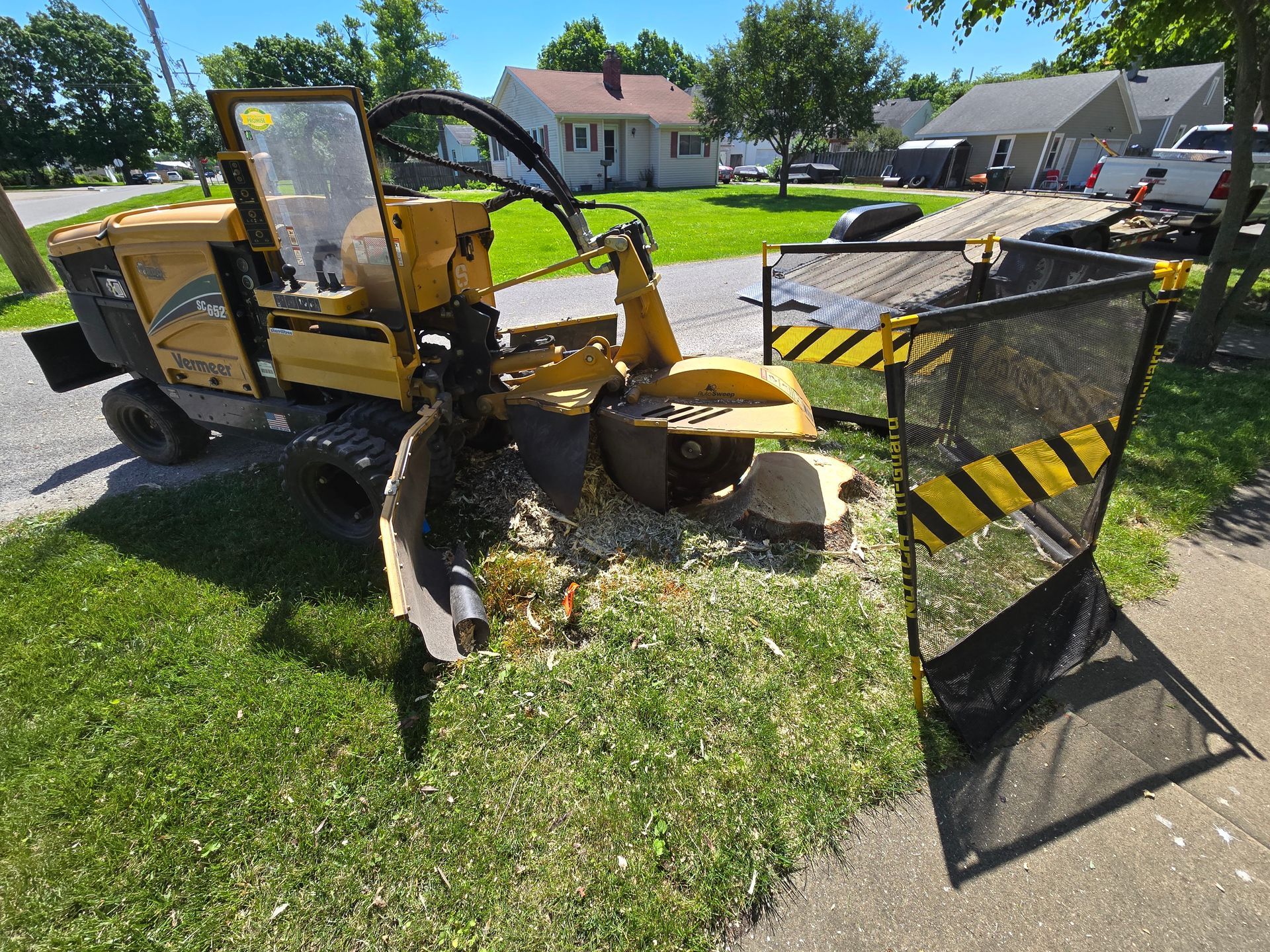 A yellow tractor is cutting a tree stump in the grass.