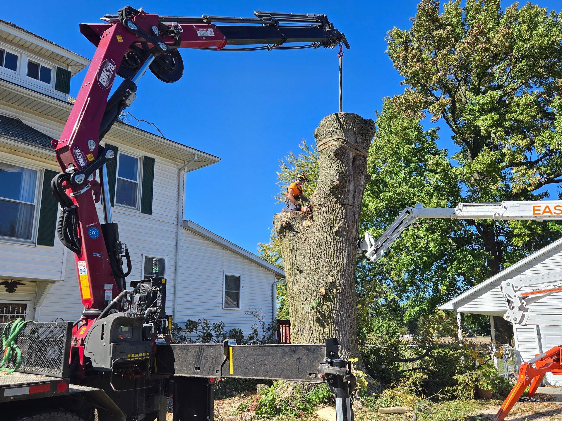 A crane is lifting a tree stump in front of a house.