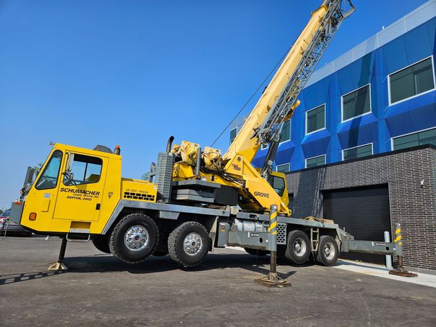 Yellow crane truck parked beside a blue industrial building with a raised boom and open gate