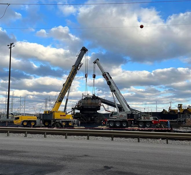 Two yellow cranes lifting equipment in a snowy industrial yard under a cloudy sky