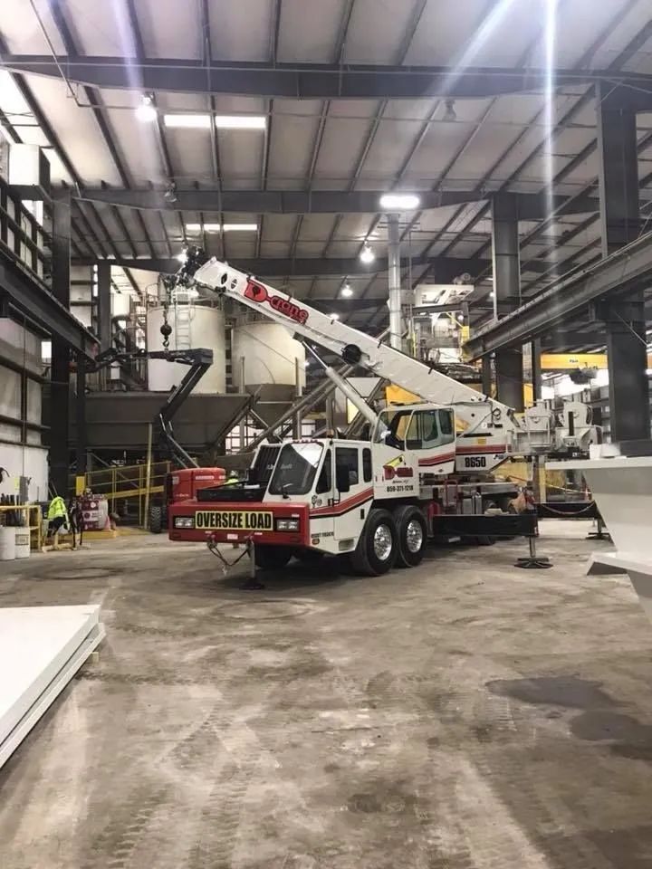 White crane truck with raised boom inside a large industrial warehouse