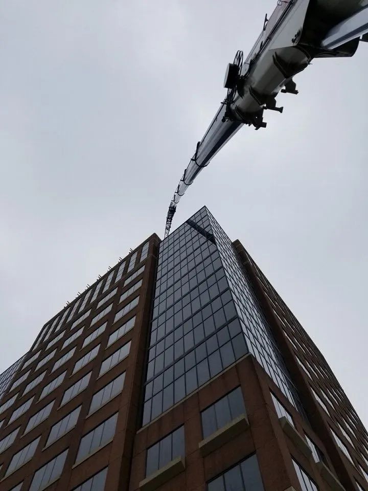 Upward view of a tall glass office building with a crane arm overhead against a gray sky